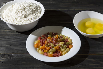 Raw colored pasta in a white plate on a wooden table