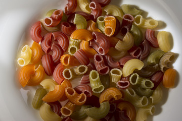 Raw colored pasta in a white plate on a wooden table