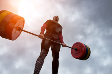 athlete have difficulty holding a heavy barbell against the sky