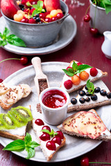 Fruit toast on red background. Healthy breakfast. Clean eating. Dieting concept. Grain bread slices with cream cheese and various fruit, berries, seeds. Vegetarian.