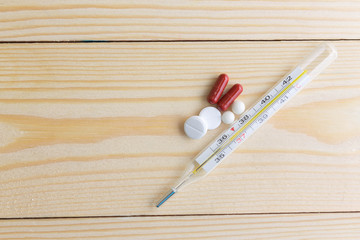 Mercury thermometer and antibiotics on a wooden table. Health and medicine.