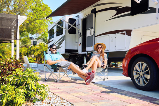 Young couple sits on chairs near camping trailer and car
