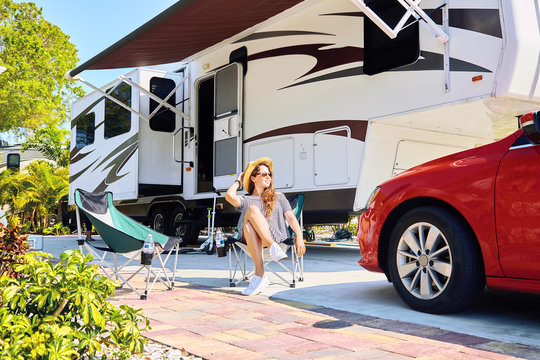 Young woman sits on chair near camping trailer and car