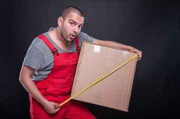 Mover guy holding box measuring with tape looking surprised