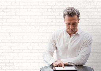 Business man at a desk looking at a tablet against white wall