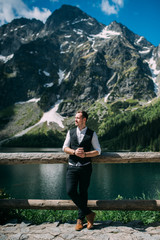 Fototapeta premium the groom stands on a background of mountains and lakes