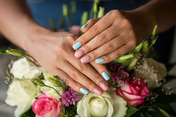 Obraz na płótnie Canvas Natural nails with beautiful manicure, pink and blue polish on women nails on blossom flowers background. Nails of woman with creative manicure near bouquet of fresh flowers