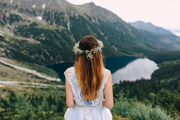 the bride in a beautiful blue dress with a deep neckline at the back with a wreath on her head of...