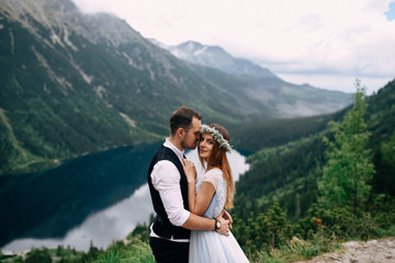 Fototapeta na wymiar bride with the beautiful blue dress and groom hugging with views of the beautiful green mountains and lake with blue water