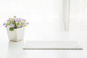 White computer keyboard on white table with purple flower on top