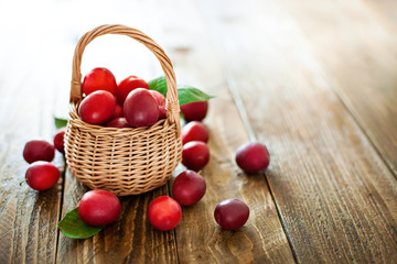 Ripe red plums in a wicker basket on a wooden table.