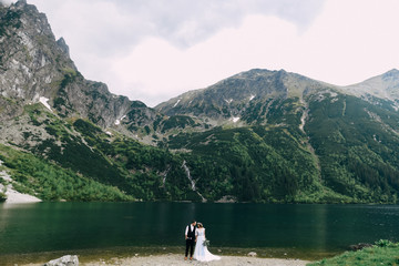 Fototapeta na wymiar bride with the beautiful blue dress and groom with views of the beautiful green mountains and lake with blue water