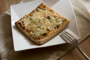 Pizza toast with cheese and fork on the white plate.
