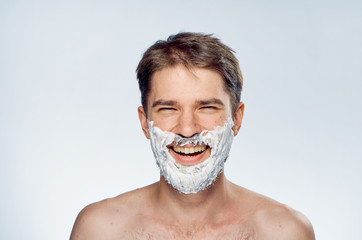 Young guy with a beard on a light background in shaving foam