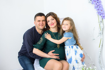 Happy family: young beautiful pregnant woman, a young man and their cute little daughter on white background
