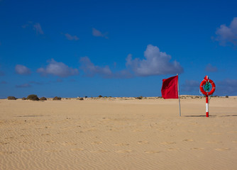 Naklejka premium Swimming circle. Life buoy red color on beach with bright sand and sky background. Two warning signs. Safety guard, lifebuoy, lifeguard. Vacation at ocean.