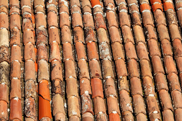 Part of tile on the roof of a house building, closeup. A red tiled terracotta roof. The orange roof tiles, maps and textures. Texture of tiles. Background with part of roof. Rows of roof bricks.