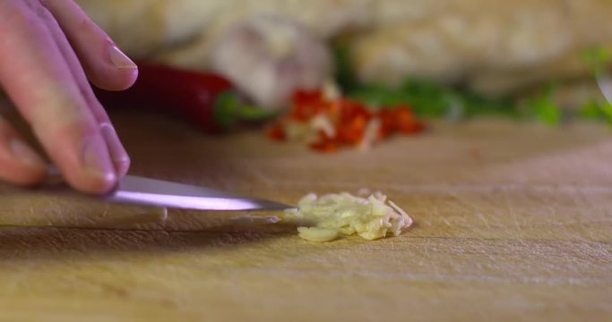 Chef uses flat blade to paste chopped garlic on wooden kitchen board. Slow motion