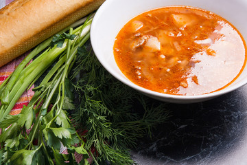 Vegetables and meat in red beetroot soup or borsch in white plate on dark marble background.
