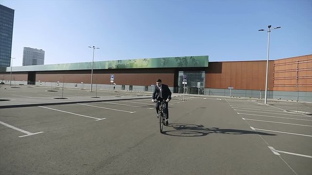 Confident young businessman in a suit rides a bicycle in the city.