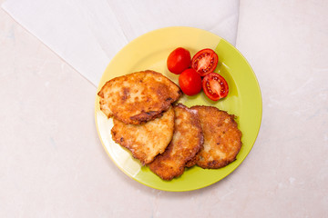Potato pancakes with meat and tomatoes on green plate in Belarusian style on light background..