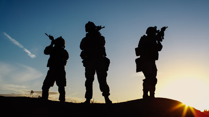 Squad of Three Fully Equipped and Armed Soldiers Standing in Desert Environment in Sunset Light.