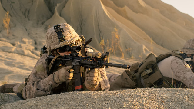 View on Soldier Lying Down on the Hill, Aiming through the Assault Rifle Scope in Desert Environment.