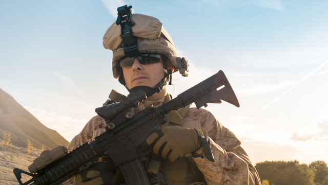 Portrait of Fully Equipped Solder Holding Assault Rifle and Standing in the Desert Environment.