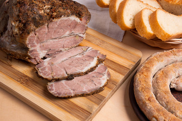 Roasted traditional homemade sausage with spices and herbs. Baked pork with herbs and spice on wooden board and and slices white wheat bread.