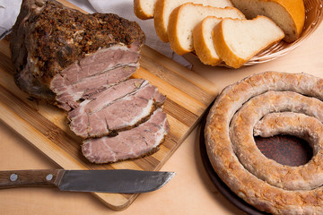 Roasted traditional homemade sausage with spices and herbs. Baked pork with herbs and spice on wooden board and and slices white wheat bread.