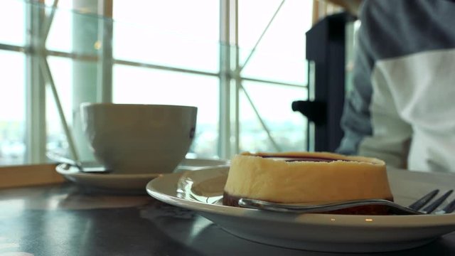 Closeup on a dessert and a cup of coffee on a table in a cafe, a man sits at the table in the blurry background