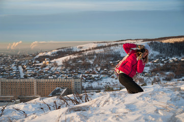 Girl tourist in a red jacket photographs the winter landscape on the camera. The tourist takes off...