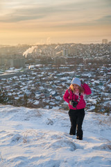 Girl tourist in a red jacket photographs the winter landscape on the camera. The tourist takes off the dawn in the morning. A girl in a gray hat takes off the morning city. Winter Saratov.