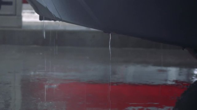 A car in a parking lot on a rainy day, raindrops trickle from the bottom down on the asphalt - closeup