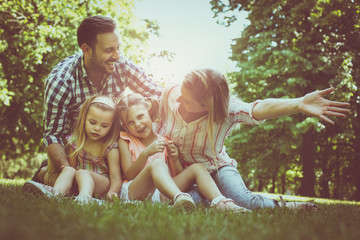 Happy family sitting on grass in the meadow together and enjoying in summer day.