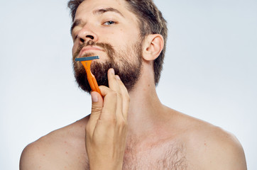 Young guy with a beard on a light background shaves