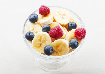 Top view of tasty breakfast of bowl with banana, blueberries and raspberries on tablecloth.