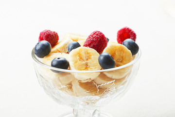 Tasty breakfast of bowl with banana, blueberries and raspberries on tablecloth.