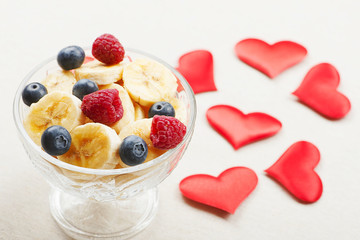 Tasty breakfast with bowl with banana, blueberries and raspberries along with hearts. Valentine's Day