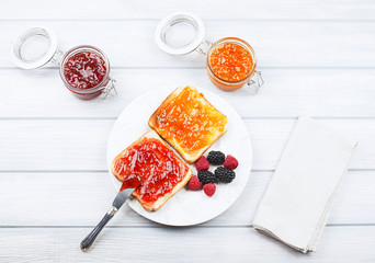 Top view of tasty toast breakfast with strawberry and peach jam along with blackberries and raspberries on wooden table.