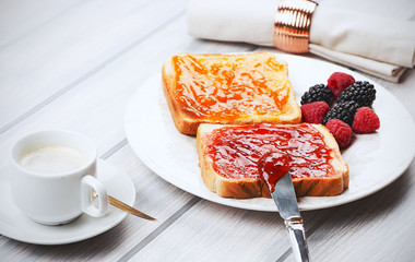 Tasty breakfast of toast with strawberry and peach jam along with blackberries and raspberries, and a cup of coffee.