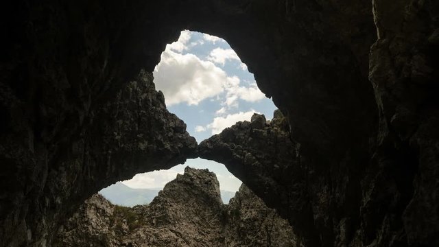 4 k timelapse shot looking up through the stone arch to the white moving clouds.  Piatra  Craiului Mountains, Romania.