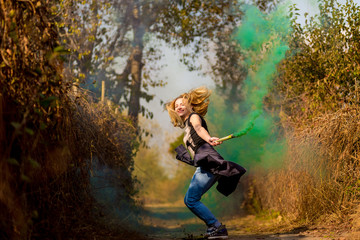 Fototapeta na wymiar Happy girl laughing and running with green color smoke bomb in forest.