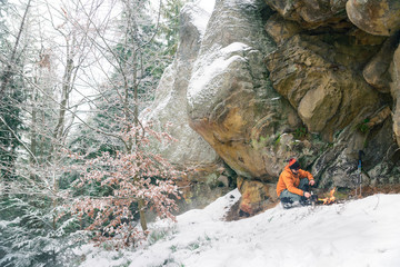 man preparing food under rock where hiding from snowstorm, survival