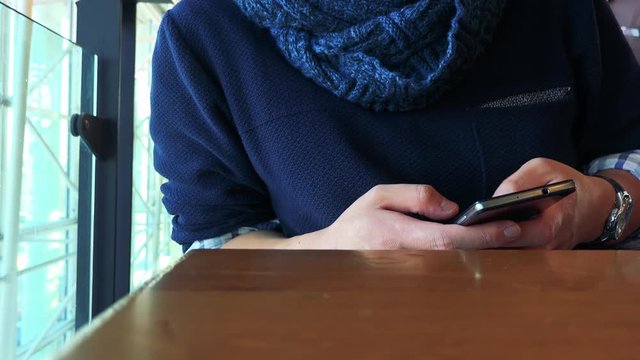 A man sits at a table by a window in a cafe and works on a smartphone - closeup