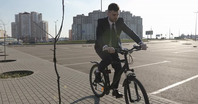 A young businessman in a suit rides a bicycle in sunny spring.