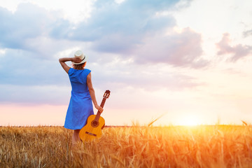 Woman musician with guitar, fields, sunset, warm summer outdoors