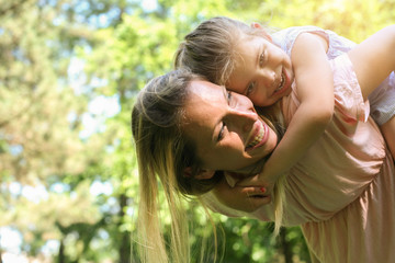 Mother and daughter outdoors in a meadow. Mother carrying her daughter on piggyback.