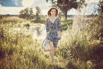 Portrait of a young beautiful girl in a long dress running along the grass against the background...