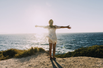 Greece, Cyclades, Naxos, woman with raised arms standing at the sea at sunset
